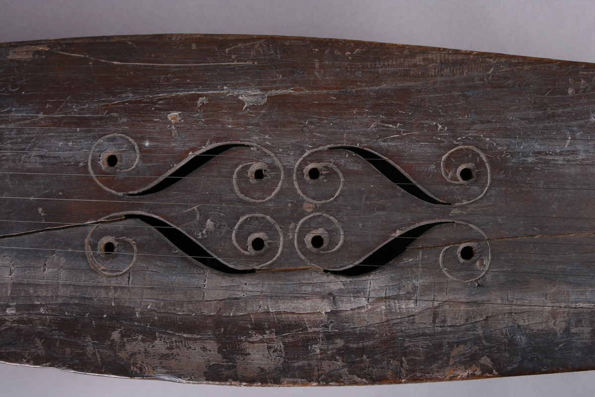 Korpus sammensatt av 4 bord, bunn og lokk limt på sidene. Lokk og bunnn i nåltre, sarger i løvtre. Hode og skruekasse i ett stykke - av løvtre. Hode i form av enkel snekke, 8 stemmeskruer. Sidene buket (Valdrestype), øvre fot mangler. 3 lydhull: 1 mindre grovt ovalt ved anslag (ant. etter kvist, (JV)), samt to par s-formet hull parvis speilvent (lager en hjerteform!).
Strengene festet i stifter like bak stol. Høyre sadel og forstykke festet til korpus med trenagler. Hele instrumentet er beiset mørk brunt. Skala på melodistrengen. Alle noter og pyramider mangler. Spor i lokket etter notene, ca 16 stk. Spor etter to strengeleder - gir korteste strenge ytterst.