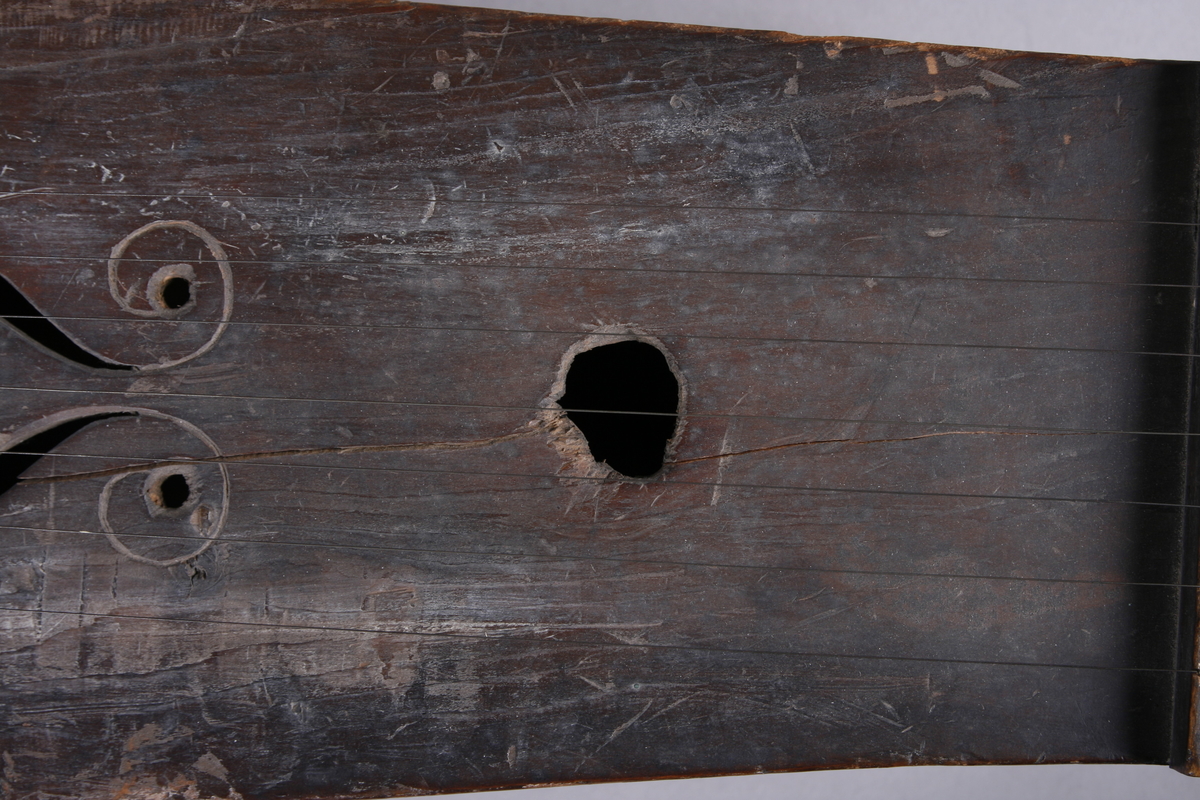 Korpus sammensatt av 4 bord, bunn og lokk limt på sidene. Lokk og bunnn i nåltre, sarger i løvtre. Hode og skruekasse i ett stykke - av løvtre. Hode i form av enkel snekke, 8 stemmeskruer. Sidene buket (Valdrestype), øvre fot mangler. 3 lydhull: 1 mindre grovt ovalt ved anslag (ant. etter kvist, (JV)), samt to par s-formet hull parvis speilvent (lager en hjerteform!).
Strengene festet i stifter like bak stol. Høyre sadel og forstykke festet til korpus med trenagler. Hele instrumentet er beiset mørk brunt. Skala på melodistrengen. Alle noter og pyramider mangler. Spor i lokket etter notene, ca 16 stk. Spor etter to strengeleder - gir korteste strenge ytterst.