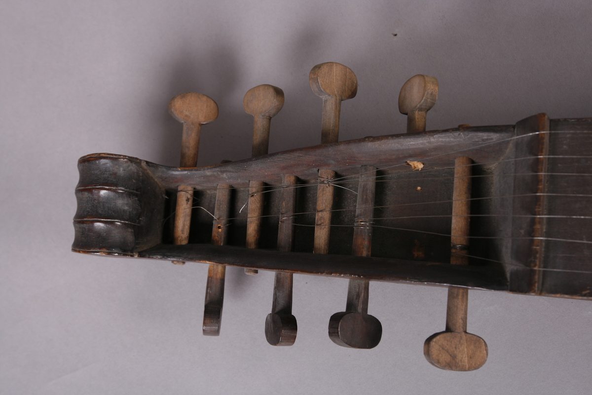 Korpus sammensatt av 4 bord, bunn og lokk limt på sidene. Lokk og bunnn i nåltre, sarger i løvtre. Hode og skruekasse i ett stykke - av løvtre. Hode i form av enkel snekke, 8 stemmeskruer. Sidene buket (Valdrestype), øvre fot mangler. 3 lydhull: 1 mindre grovt ovalt ved anslag (ant. etter kvist, (JV)), samt to par s-formet hull parvis speilvent (lager en hjerteform!).
Strengene festet i stifter like bak stol. Høyre sadel og forstykke festet til korpus med trenagler. Hele instrumentet er beiset mørk brunt. Skala på melodistrengen. Alle noter og pyramider mangler. Spor i lokket etter notene, ca 16 stk. Spor etter to strengeleder - gir korteste strenge ytterst.