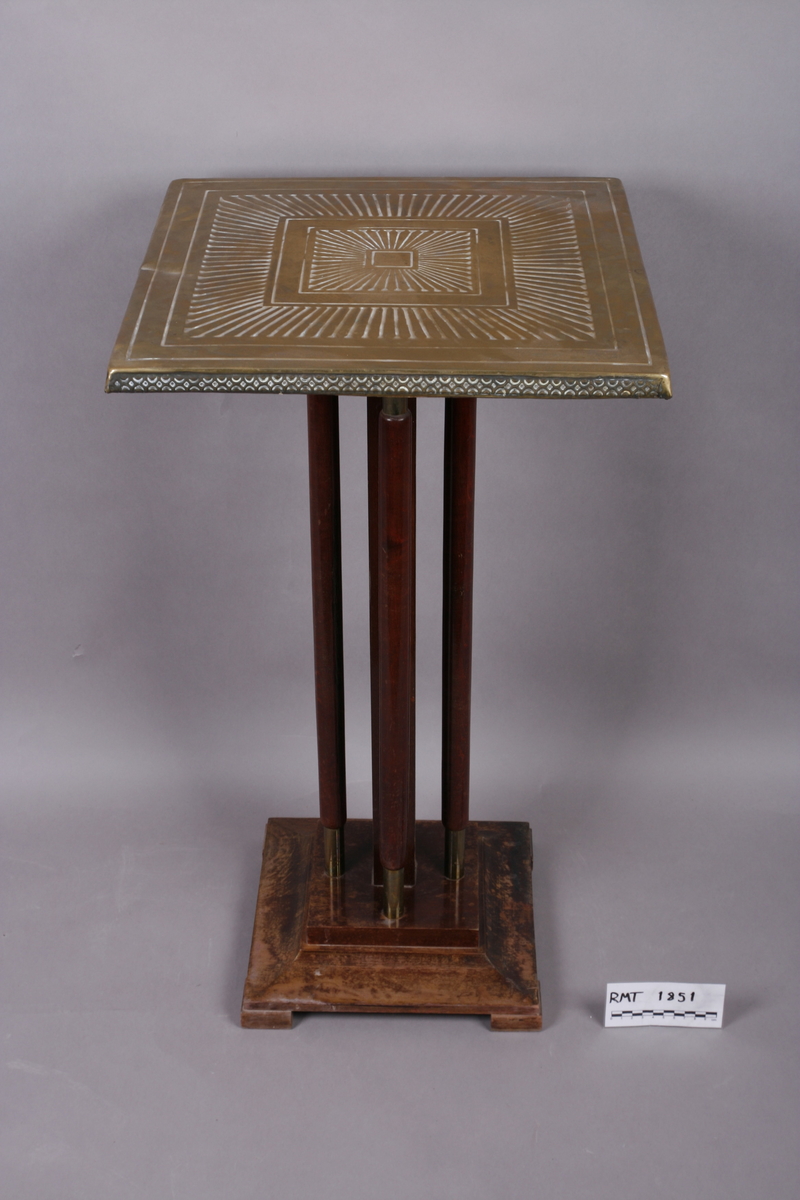 Firkantet med fire søyleben. Bordplate i messing med preget dekor.