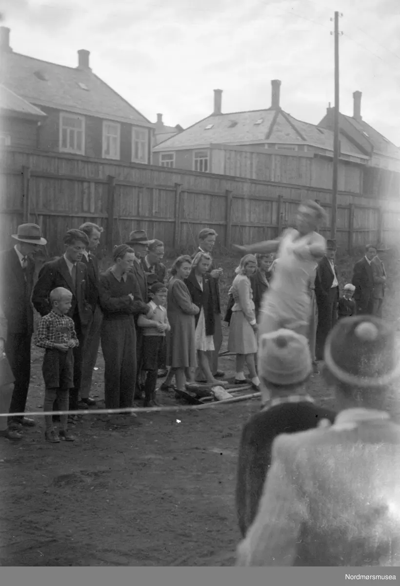 Idrettsplassen på Kirklandet i Kristiansund, Man ser husene i Fløyveien i bakgrunnen. (Info: Tor Aage Dyrseth Zdrinka) - et idrettsarrangement;  lengdehopp. Førkrigs? Bildet er fra fotosamlingen til familien Røv på Meisingset i Tingvoll kommune.  Eier av originalmaterialet er Jan Harry Røv. Fra Nordmøre museums fotosamlinger.