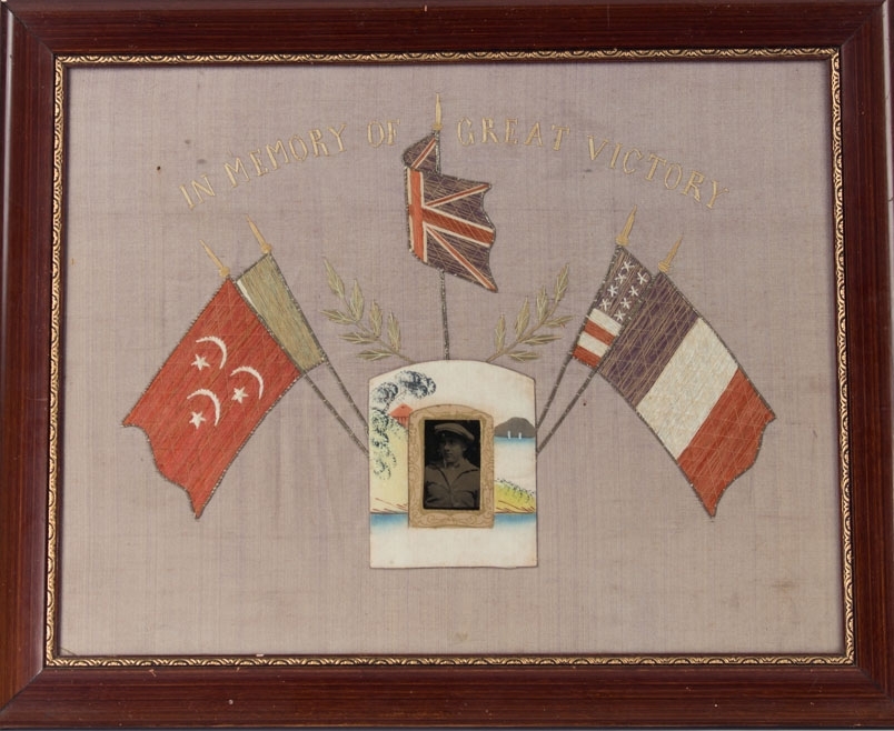 Brodert silkebilde med fotografi av ung mann. Midt i motivet fem ulike flagg som dekor rundt fotografiet. Fransk flagg, amerikansk flagg, Storbritannias flagg og trolig Ottomansk flagg (halvmåne og stjerner).