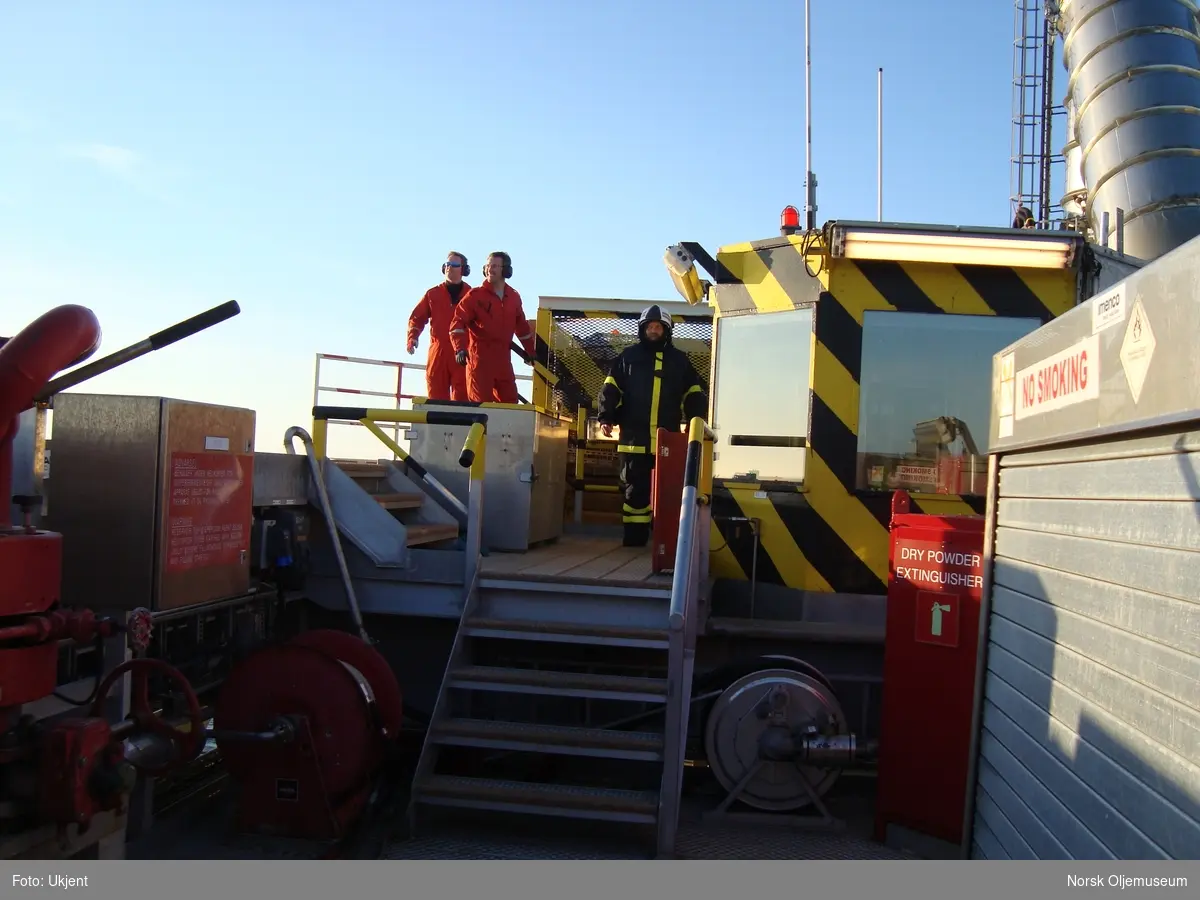 Et helikopter skal inn for landing på Draugen og helikoptermannskap og en brannmann gjør seg klar.