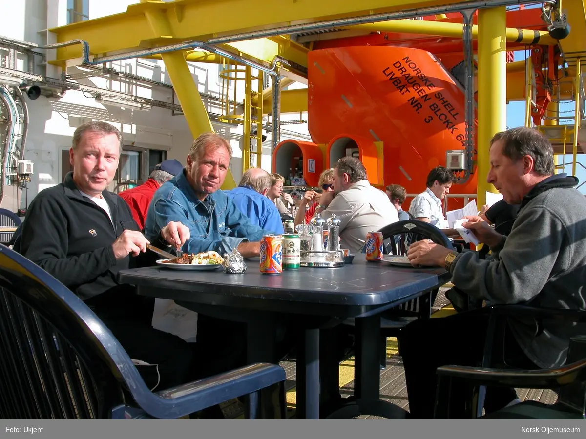 Grillfest på Draugen.  Serveringen foregår på livbåtdekket hvor det er satt opp bord og stoler.