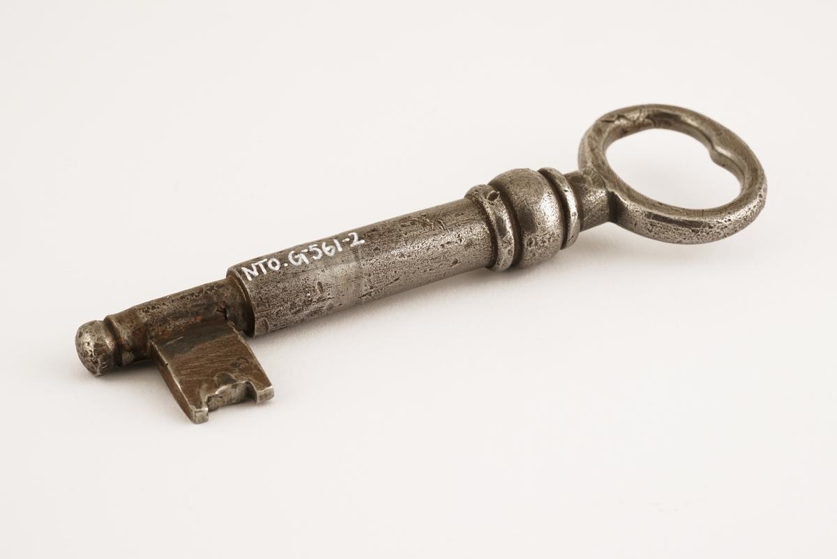 Dørlås for innmontering i dør av jern. Det medfølger tre monteringsbraketter, som selve låsen har vært montert på. Låskassen er rektangulær, med avrundede hjørner på den ene siden, og et større, flatt jern på den motsatte siden.Nøkkel følger med