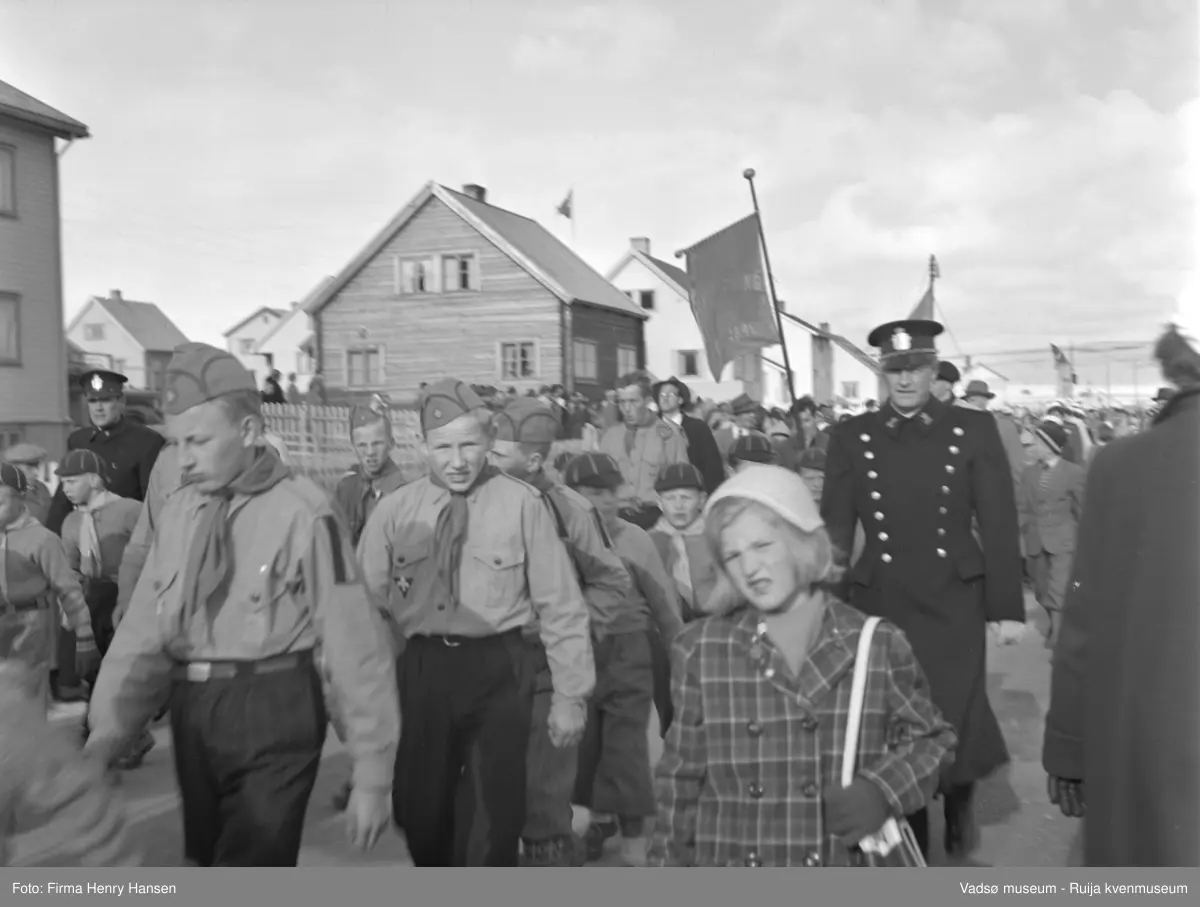 Vadsø 17 mai 1952. 17.mai-toget går gjennom Oscarsgate fra øst mot vest. Ser fjellet Melkevarden i bakgrunnen. Speidergutter og "ulvunger" i uniform. Politimann, faner lenger bak i toget.