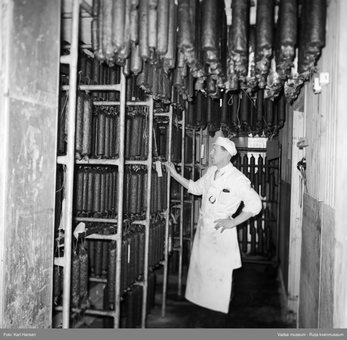 Nord-Norges salgslag Vadsø, 1964. Spekepølser i røykeriet/modneriet (klimarom). Avbildet person; produksjonsleder Hans Petter (HP) Hansen.