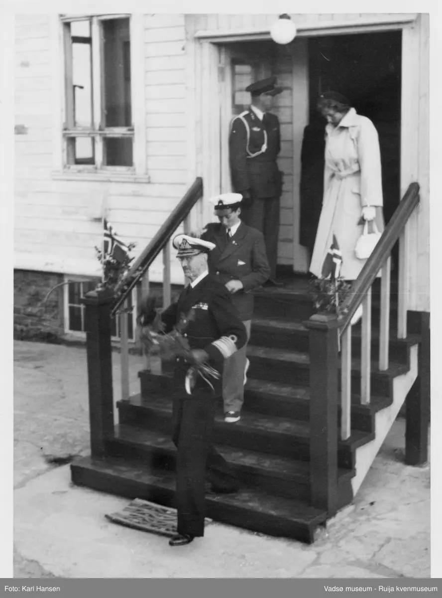 Kongebesøk i Vadsø 1950. Kong Haakon 7. og prins Harald går ned trappa. Kong Haakon og kronprinsfamilien besøkte Vadsø 25.-26.7.1950 i forbindelse med en større rundreise i Nord-Norge sommeren 1950. Under besøket sto "biltur gjennom byen" og "besøk på sykehuset" på programmet.   Kilde: Det kongelige hoff, Arkivet