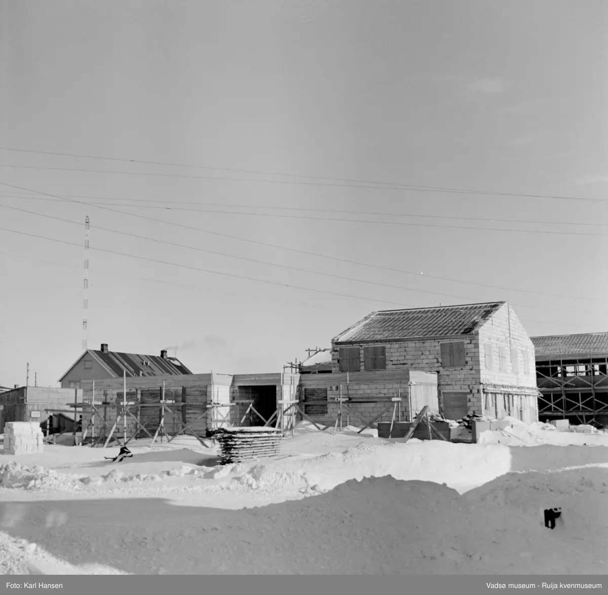 Vadsø 1962. Bildet tatt mot nordøst. Bolig for fylkesmannen under oppføring i krysset Damsveien/G. Gulliksens gt. I bakgrunnen administrasjonsbygget for fylkesadministasjonen (nå Statens hus) også under oppføring. Forskalingsmaterialer.