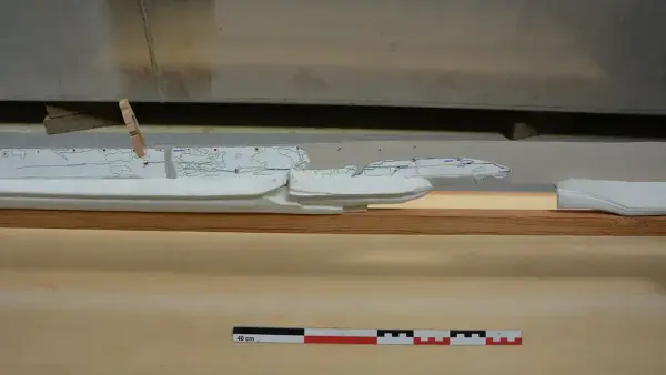 Nærbilde av 3D-printede kjøldeler i hvit plast montert på treramme. Et av kjølbordene i papp er også montert på babord side av kjølen.