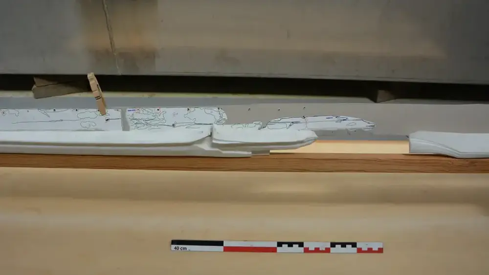 Nærbilde av 3D-printede kjøldeler i hvit plast montert på treramme. Et av kjølbordene i papp er også montert på babord side av kjølen.