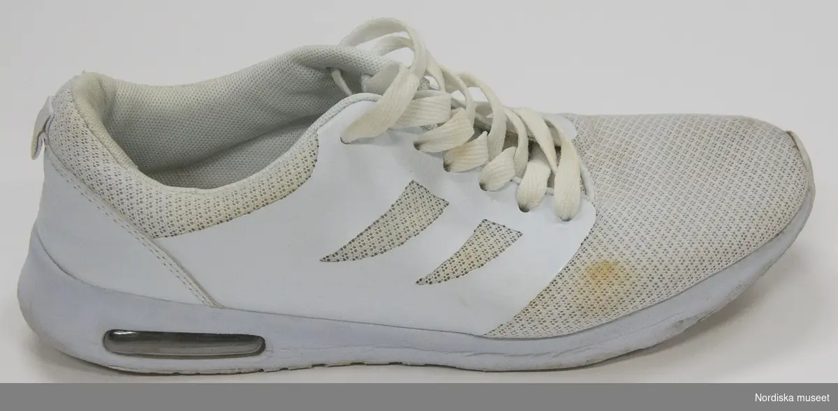 Ett par vita sneakers. Sula av plast (phylon och TPR=ThermoPlastic Rubber) med transparent plastbit under i hälen. Överdel av syntettyg och läderimitation. Snörning med vita platta skosnören genom sju par hål. Plös. Insida av syntettyg. Liten bandögla på bakkappan. 
På plösen etikett med text: 
"157 SOULS
STYLE: O2/A Shoe
SIZE: EU 45
SIZE: EU 11
MADE IN CHINA"
På innersulan svart text: "...157 SOULS".

Anmärkning: text delvis bortnött på innersulan. Bruna fläckar på ovansidans främre del.
/Leif Wallin 2017-06-07