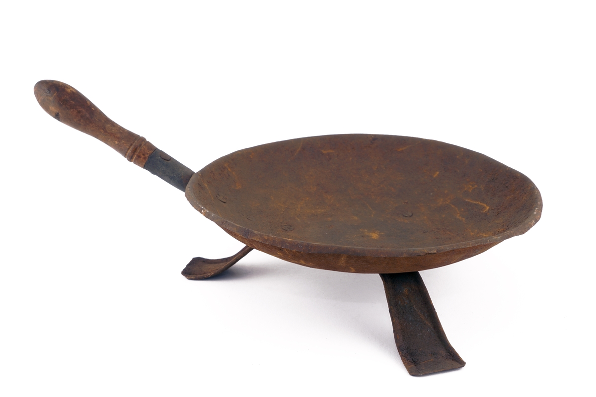 Panne av metall med trehåndtak på trebenet fot av bøyet blikk