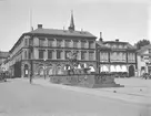 Parti av Linköping omkring 1935. Vy över Stora torget mot väster. I förgrunden breder Carl Milles Folkungabrunn ut sig sedan 1927. I byggnaderna i fonden drev vid tiden de för äldre linköpingsbor välkända affärsrörelserna Sahlströms bokhandel och Axel Peterzéns manufaktur.