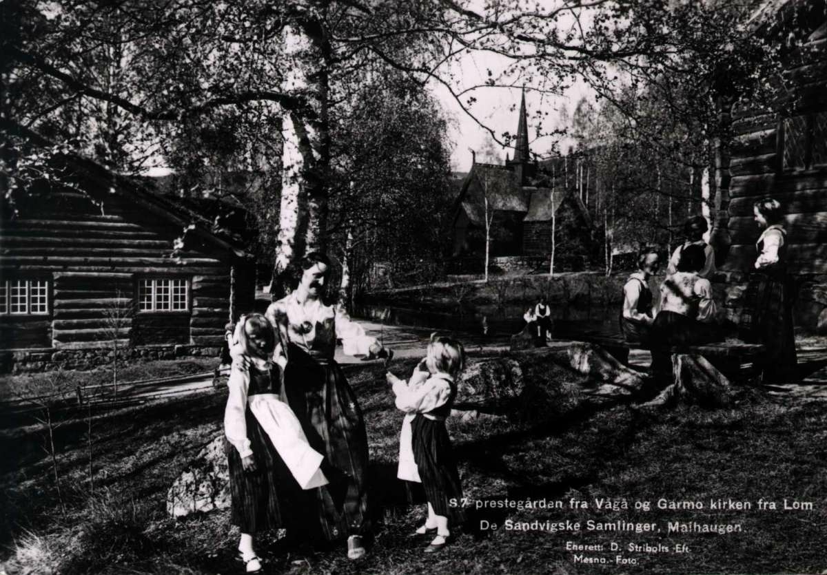 Postkort. Jule- og nyttårshilsen. Fotograisk motiv.  Svart/hvitt.  Fra de Sandvigske Samlinger på Maihaugen. Bunadkledde barn og kvinner. Kirke. Avsender: Anders Sandvig. Stemplet julen 1945.