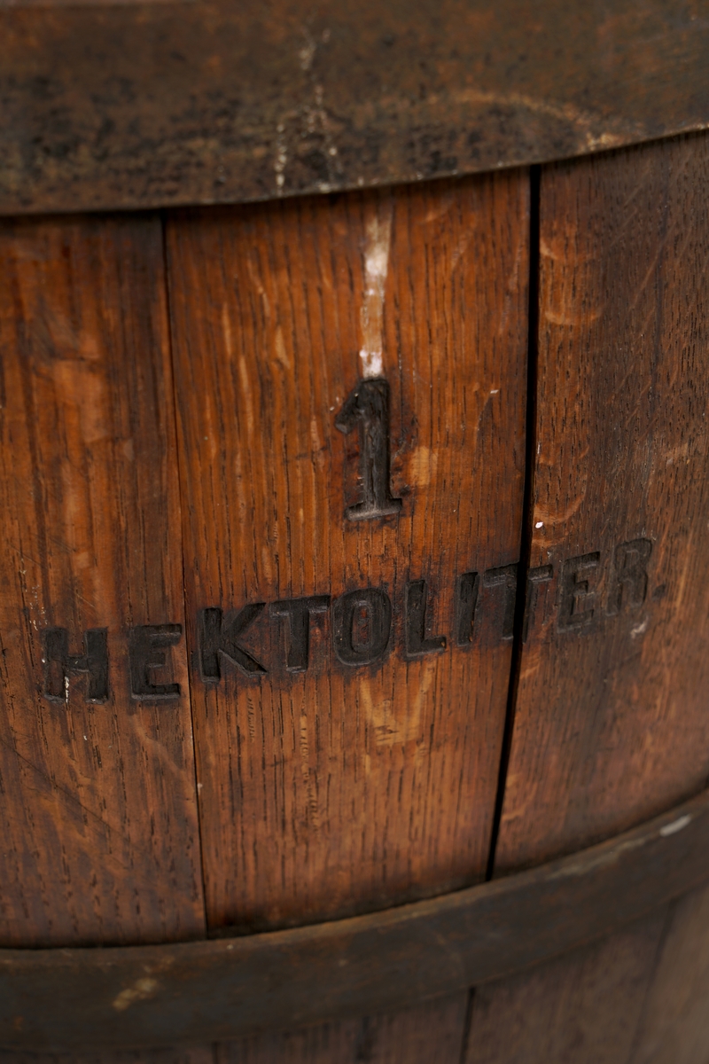 Tretønne (hektolitermål) med 2 bærehanker av metall,.Tønnen er utvendig forsynt med fire metallringer.