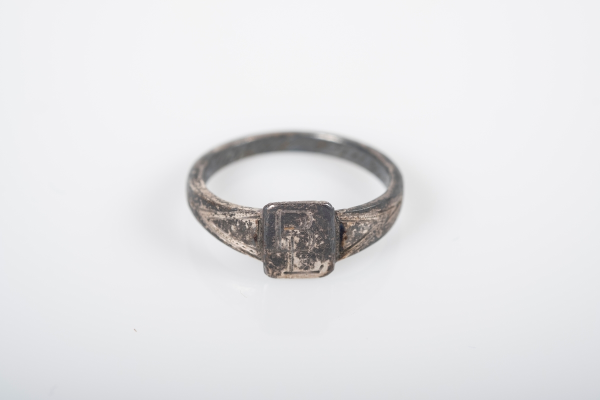 Liten rund ring med et firkantet monogram foran med initialene BL inngravert. På innsiden er det inngravert "Fra Far Grini 1942-43".