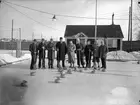 Nio curlingspelare, i bakgrunden syns klubbstugan. Från vänster: Hans Thermaenius, Bengt Thermaenius, Carl Norberg, Gottfrid Thermaenius, Rune Dahlman, Olle Thermaenius, Hugo Wilsson, Olle Berglund, Erik Berglund.
Eyravallen, Örebro.