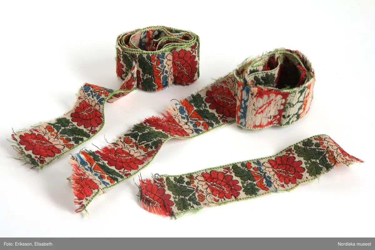 Huvudliggaren (år 1883):
"35.726 Brudgumsdräkt fr. Toarps sn. Ås hd. Västergötland. a. Blå långrock, med broderi i silke. b. Röd toppmössa; till mössan hör en tofs i toppen. c. Väst, troligen begagnad som tröja. d. Blå knäbyxor. e. Strumpeband. Till banden höra runda tofsar. 'Dräkten är från början af detta århundrade.'; Se bref från Södermark 21/5 1883. a. Maläten. d. Maläten. e. Maläten. 'I dräkten saknas: strumpor, hvita eller blå, skor, helst med spännen, bomullshalsduk, skjorta.' Se bref från Södermark af den 22/5 1883. G. af handlanden Oscar Vennberg i Borås genom lant [?]kamrer I.A. Södermark i Borås 23/5 1883. Bil. Södermark."