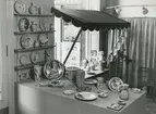 Interiörbild. Utställning med föremål från Gustavsbergs fabriker. Fat och vaser. Fajanser målade i rödlera, polykrom dekor. Konstnärer: Wilhelm Kåge och Stig Lindberg. 1942. Plats okänd.