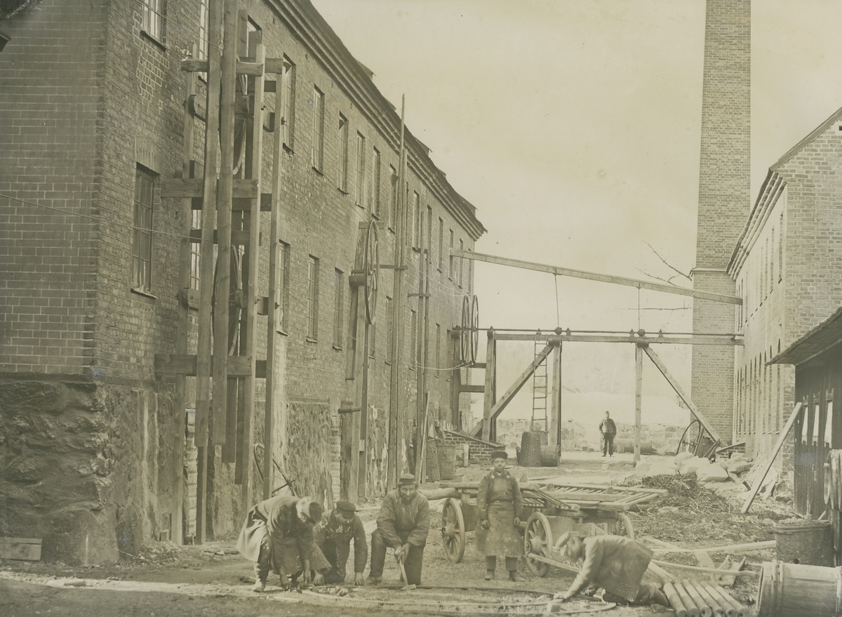 Exteriör. Vy över Gustavsbergs fabriksområde.  Slamhusgatan sedd från söder. Gamla verkstaden från 1852-53 t.v. Slamhuset. Bilden visar  även hjul och transmissionsaxlar.
Personer: okända