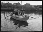 Fyra kvinnor i en roddbåt. Ankrade fiskebåtar i bakgrunden. Troligen Fiskebäckskil, Bohuslän.