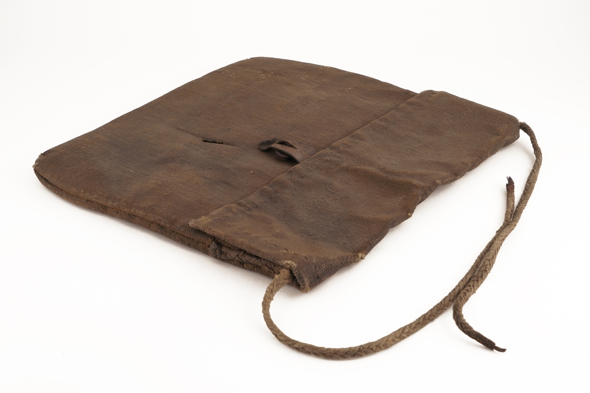 Veske av oljet seildukstekstil (i henhold til tidligere registrering), hvor lokket låses med rem av lær med knappehull og knapp av antatt tre festet på vesken.. En bærestropp av flettet tekstiltau er sydd fast i begge ender på veskens bakside. Tauet har røket.