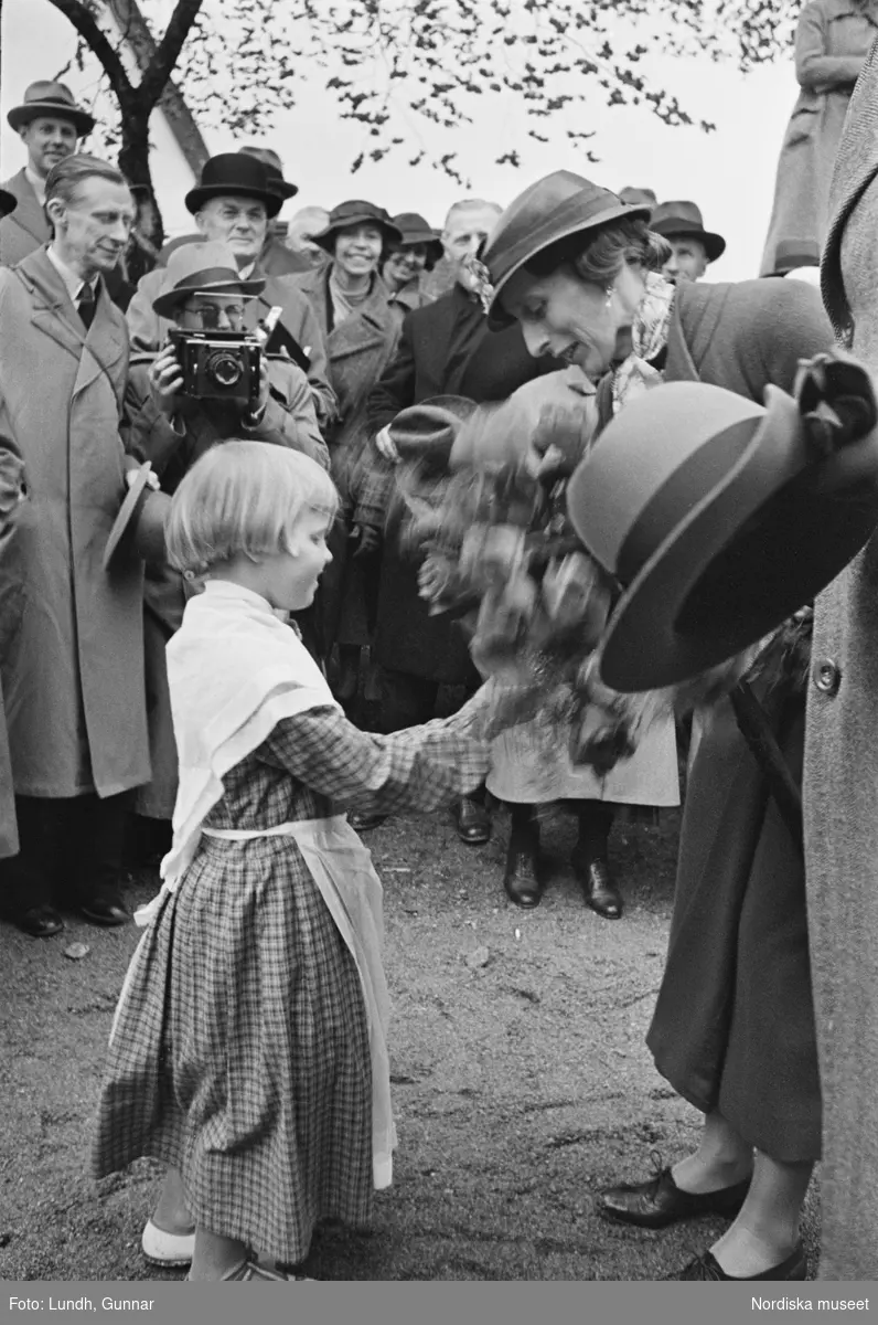 En liten flicka räcker över en blomsterbukett till kronprinsessan Louise vid en hembygdsfest i Härkeberga.