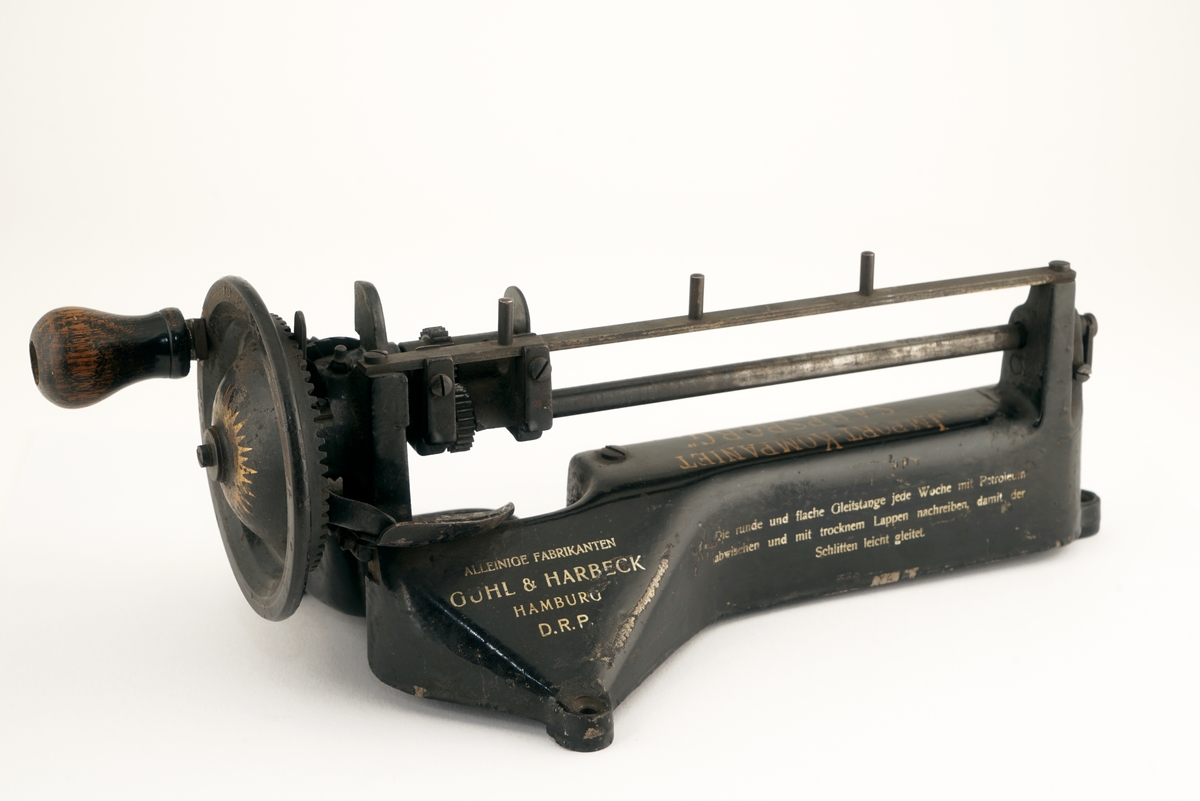 Blyantspissemaskin  av metall, sortlakkert med påskrift i gullfarge. Dreiet trehåndtak.