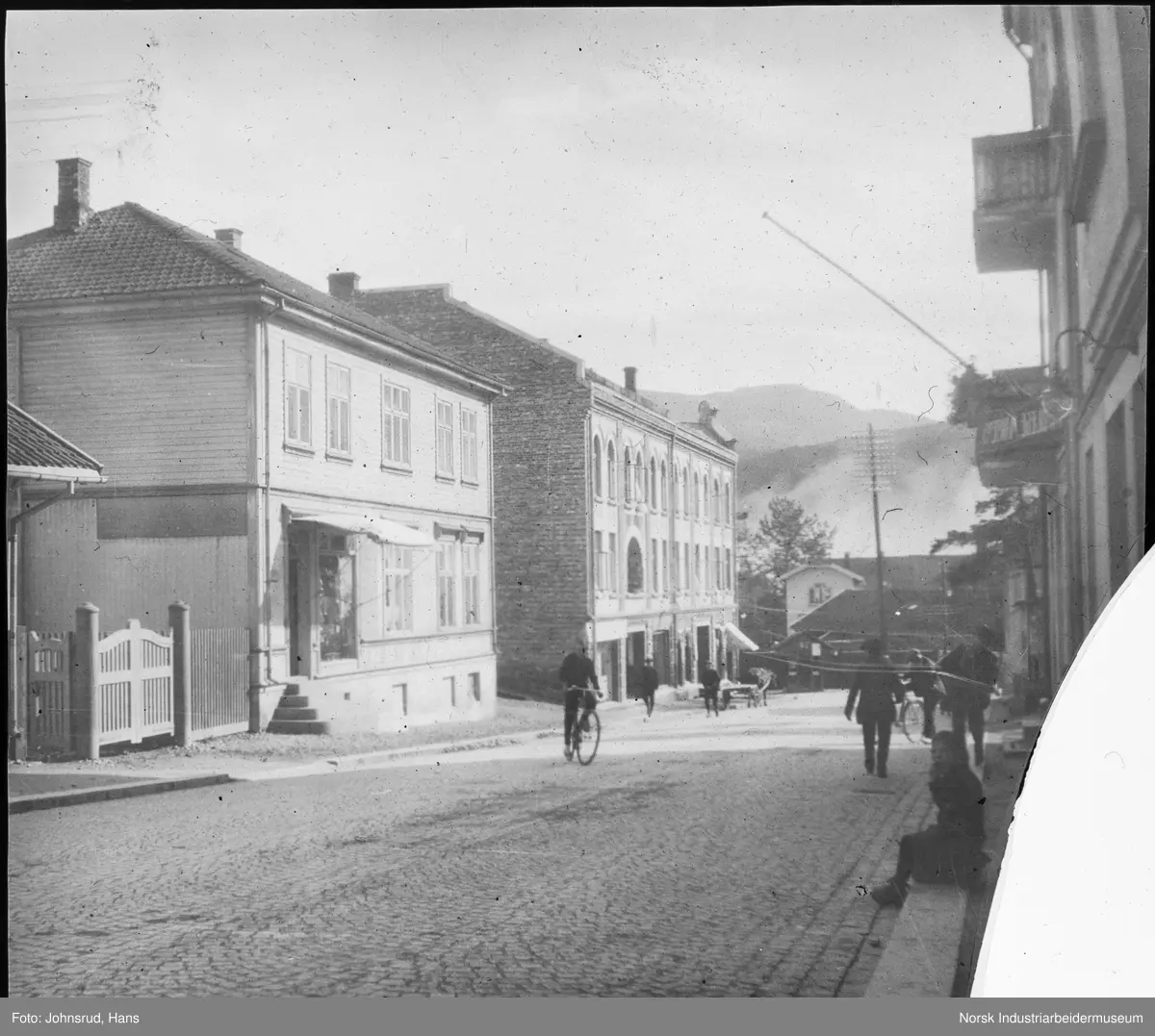 Gatemiljø i Storgata i Notodden. Gaten er brosteinsbelagt, butikklokaler langs gata. Mennesker gående og syklende.