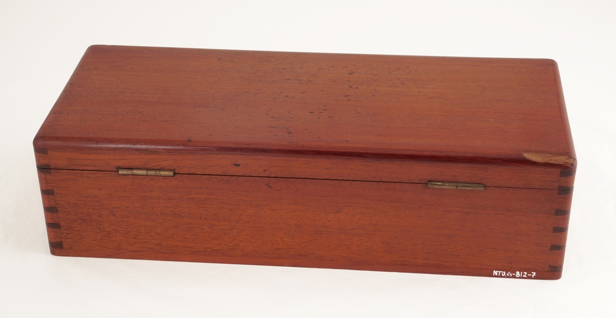 Trekasse med lokk med to låser med hver sin nøkkel. Inneholder to runde messingbeholdere, hvorav én med skrulokk, besatt med lær og med glassbeholder for fargestoff inni . Den andre med vanlig lokk, med stempelpute inni. Kassen inneholder i tillegg en børste med håndtak av tre,  ett stempelverktøy av tre, en glassflaske med kork inneholdene fargestoff, samt en rektangulær metallbeholder med skrukork.