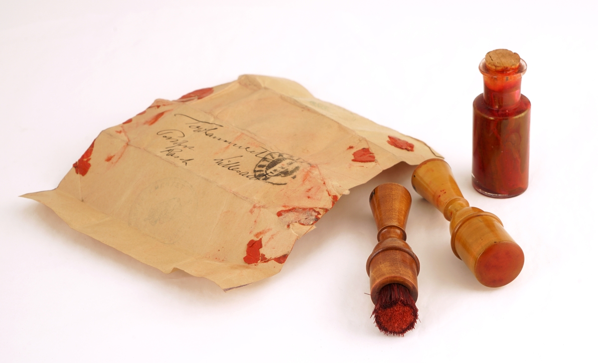 Trekasse med lokk med to låser med hver sin nøkkel. Inneholder to runde messingbeholdere, hvorav én med skrulokk, besatt med lær og med glassbeholder for fargestoff inni . Den andre med vanlig lokk, med stempelpute inni. Kassen inneholder i tillegg en børste med håndtak av tre,  ett stempelverktøy av tre, en glassflaske med kork inneholdene fargestoff, samt en rektangulær metallbeholder med skrukork.