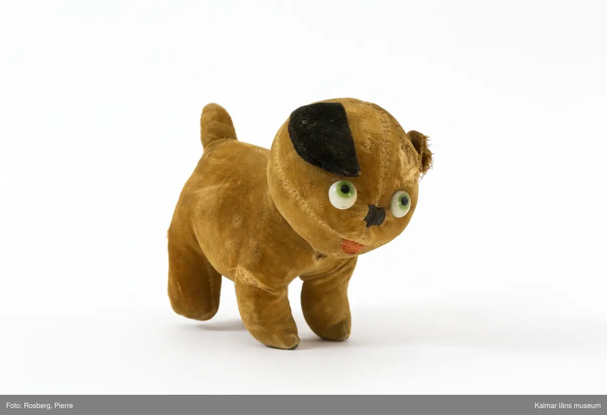 KLM 32005 Hund, leksakshund av stoppad plysch. Brun med ett svart öra. Ett öra saknas. Påklistrade plastögon.