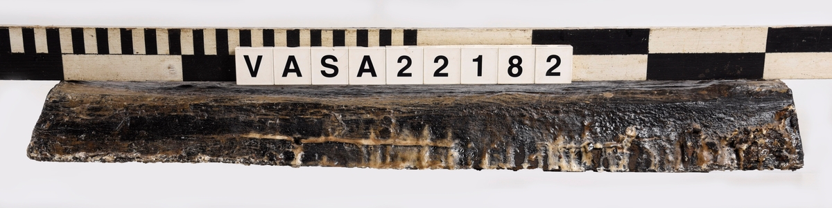 Tröskel till kanonport 14. Nästan rektangular med fasad kanter och ändar. 6 moderna skruvhål, ett klart original spikhål och ett till möjligt.
Lite deformerad, mycket vittrad på ytor (ändar bättre bevarad).