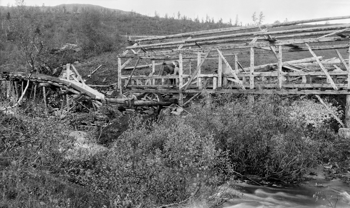 Bygging av sirkelsag ved Åkervika i Hattfjelldal på Helgeland.  Vassrenna kommer inn ved venstre bildekant mot ei ramme der det var opplagret en askling med underfallshjul og reimskive.  To menn arbeidet med sagbenken under det ennå ukledde og utekkete bindingsverket som skulle bli saghus. Saga lå i ei li der det vokste bjørkeskog.