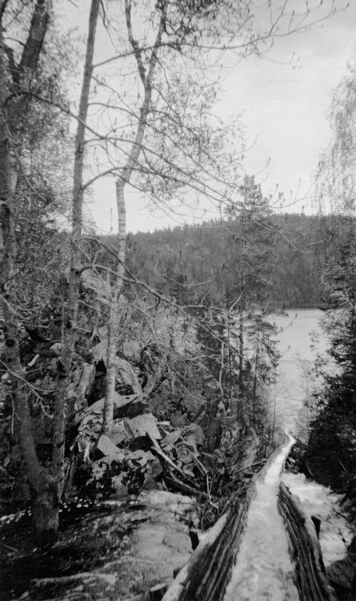 Fløtingsrenne i Krokvannsvassdraget i Henseid i Telemark.  Fotografiet viser tømmerrenna mellom Fløsetdammen og Henseidvatnet.  Fotografiet er tatt fra en posisjon over renna, i medstrøms retning.  Vi ser også noe av den flomstore åa renna henter vann fra.  Det bergfylte terrenget til venstre i fotografiet utløser tanker om hvor vanskelig det ville vært å fløte her om man ikke hadde hatt tømmerrenne.  I bakgrunnen skimtes vannspeilet på Henseidvatnet og en bakenforliggende, skogkledd ås. 