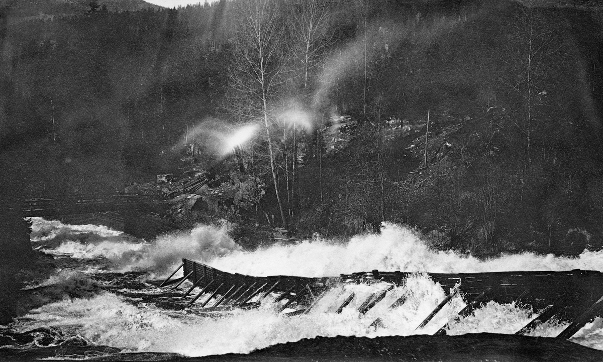 Tømmerrenne ved Sølverødfossene i Siljan.  Englandskap med elv som kommer fra skogen i bakgrunnen, tømmerrenne i den øvre delen av fossen, småbruk og granskog i bakgrunnen. 