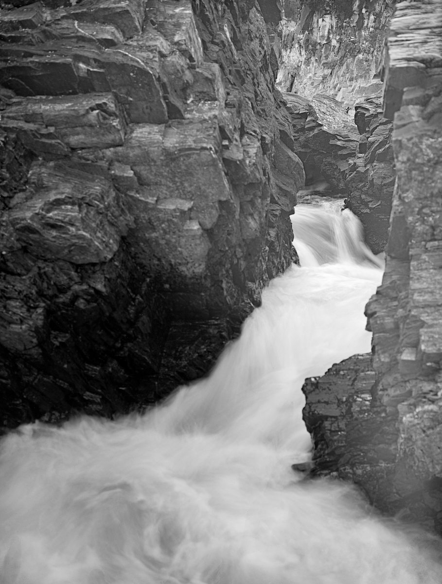 Fra laksetrappa i Forsjordfossen i Vefsna i Nordland. Dette fotografiet er tatt i motstrøms retning. Laksatrappa er sprengt ut i fjell på høyre side av fossen. Stedet ble valgt fordi terrenget på den andre sida av fossen var slik at det ville blitt vanskelig å skjerme fisketrappa for fløtingstømmeret i vassdraget. Dette skulle vise seg å by på visse problemer også i den traseen som først ble valgt. Arbeidene med laksetrappa ved Forsjordfossen ble påbegynt vinteren 1886-87. Man satset i første omgang på å bygge den slik at man utnbyttet en naturlig kulp i fossen og å supplere den med et par utsprengte dammer, som ble forbundet med smalere renner. Det viste seg raskt at laksetrappa ikke gav den oppgående fisken nødvendig skjerming. Følgelig gav man seg i kast med en ny løsning, der man bygde videre på den nederste delen av den første trappa som var utminert, men fortsatte mineringsarbeidene videre oppover med sikte på at laksen skulle skjermes helt til den nådde oversida av fossen. Arbneidet ble utført vinterstid - da det var lav vannføring - over to-tre år. Fra 1890 var fisketrappa ved Forsjordfossen effektiv. Dette skapte nye muligheter for utleie av attraktivt laksefiske for ovenforboende grunneiere, noe som inspirerte til trappebygning også i de ovenforliggende fossene, der med betydelige økonomiske bidrag også fra grunneierne. Laksetrappa ved Forsjordfossen ble, på grunn av alt mineringsarbeidet, en ganske kostbar affære for staten, særlig med tanke på at fallhøyden på dette stedet bare var på cirka 3,5 meter.

En samtidig rapport om bygginga av fisketrappa i Forsjordfossen finnes under fanen «Opplysninger».