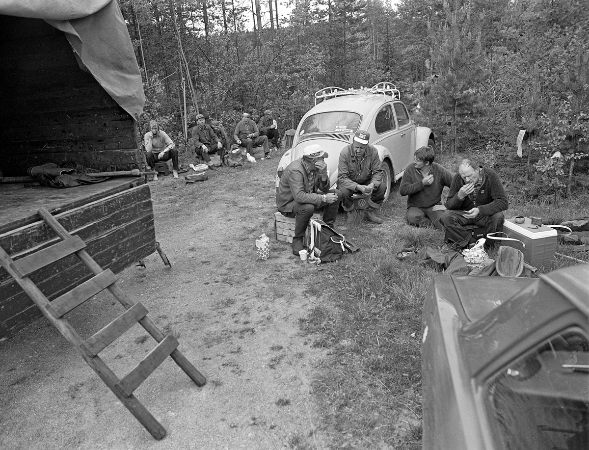 Fløterlaget som fløtte tømmer i elva Søndre Osa i Åmot i 1981, fotografert under ei matpause ved Kvernfallet. Paul Solberg fulgte karene i en liten lastebil etter hvert som de arbeidet seg nedover elveløpet. Lastebilen transporterte utstyr og mat, og Pauil Solberg kokte bålkaffe på høvelige kvilesteder. Her satt karene på kasser, som antakelig også hadde fulgt med lastebilen, mens de spiste brødskiver, drakk kaffe og røykte. I den bakerste gruppa gjenkjennes Odd Risberget og Harald Øren fra Osen. Deretter følger en foreløpig ukjent kar og Odd Nordnes, som også bodde i Osen. I den fremste gruppa sitter Arne Norsted fra Osen til venstre.  som også var fra Osen. Arbeidskameraten han snakket med er foreløpig uidentifisert. Deretter følger Dag Tore Syversen fra Åsnes og Nikolai Myrene fra Osen. Vi ser bakparten på den nevnnte lastebilen til venstre i bildet. Ellers ser vi ei Folkevogn-boble (som kan ha tilhørt fotograf OT Ljøstad) og litt av en Opel kadett (helt til høyre).