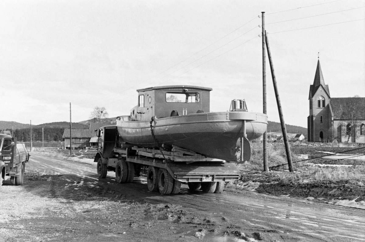 Transport av varpebåten «Varp I» fra Fetsund til Ullern ferjested i Sør-Odal, Hedmark.  Fotografiet er tatt skrått bakfra slik at akterenden på båten og styrhuset trer godt fram, mens lastebilen kommer mer i bakgrunnen.  Båten ligger på et plan som antakelig ellers ble brukt til transport av anleggsmaskiner, men på et provisorisk underlag av tre som er avpasset etter skroget, slik at fartøyet ikke skulle vippe på kjølen når bilen kjørte på svingete veg.  Transporten er fotografert på en grusveg som er preget av vårløsning.  Spedisjonsfirmaet P. Nielsen fra Oslo sto for transporten.  Til høyre i bildet ligger ei teglsteinskirke, antakelig Ulleren kirke.  Til venstre skimtes deler av en noe mindre lastebil. 

«Varp I» eller «VB 51» ble bygd for Christiania Tømmerdirektion i 1914.  Båten ble i hovedsak bruk på Glomma i nedre Solør og framfor alt på Storsjøen i Odalen.  Den hadde sitt opplagssted på Bukkeneset i Nord-Odal.  Der ble det opprinnelige overbygget, motoren og vinsjen fjernet like før jul i 1954 (jfr. SJF.1990-02242 og SJF.1990-02243).  Så ble skroget kjørt til lenseanlegget ved Fetsund i Akershus, hvor båten ble ombygd og modernisert, før den altså ble sjøsatt ved Ullern ferjested påfølgende vår for fortsatt bruk i fløtinga i den nevnte regionen. 

Lastebilen som ble brukt til dette transportoppdraget hadde registreringsnummer A-48547 og var en såkalt FWD SU-COE.  Dette var en amerikansk lastebilmodell - chassisene ble produsert ved FWD-fabrikken i Clintonville i Wisconsin (USA).  Derfra ble de sendt til Wilson Motor Bodies i Kitchener i Ontario (Kanada), hvor førerhuset og andre påbygningsarbeider ble utført.  Slike kjøretøyer ble levert til den amerikanske hæren i 1940-åra, og en del av dem kom til Europa som ledd i det amerikanske gjenreisingsprogrammet etter 2. verdenskrig.