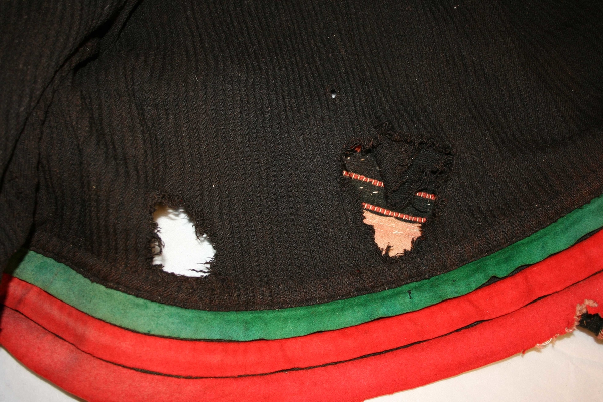 Stakk av svart vadmål i tradisjonell form. Brodert opplut, faslar og  line. Svært dårleg stand, med fleire store hol. Falma.