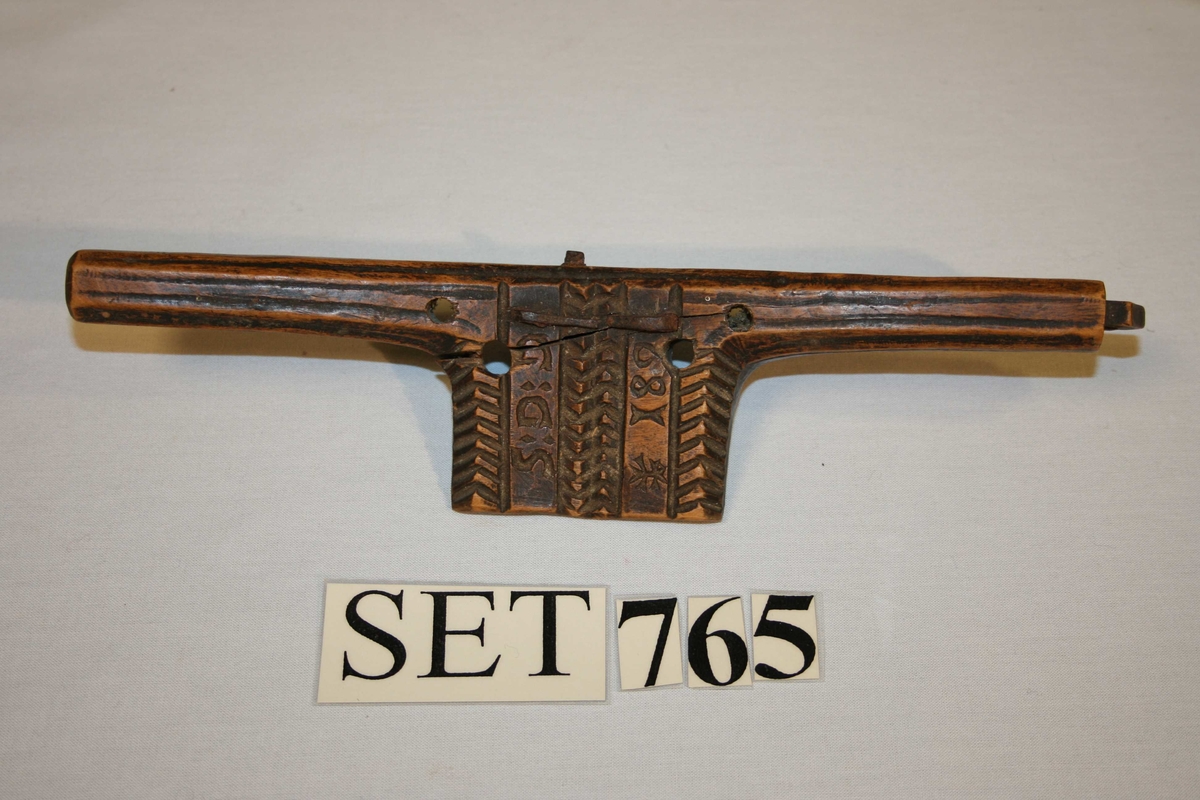 Trestykke med eit handtak i kvar ende, Eggjern  med profilar midt på. Pynta med profilar og border. Jernet rusta, treet sprekt.