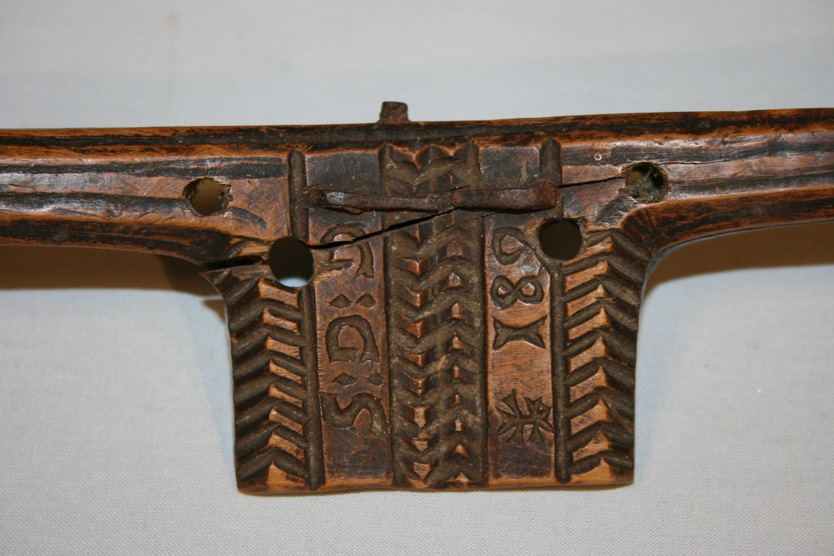 Trestykke med eit handtak i kvar ende, Eggjern  med profilar midt på. Pynta med profilar og border. Jernet rusta, treet sprekt.