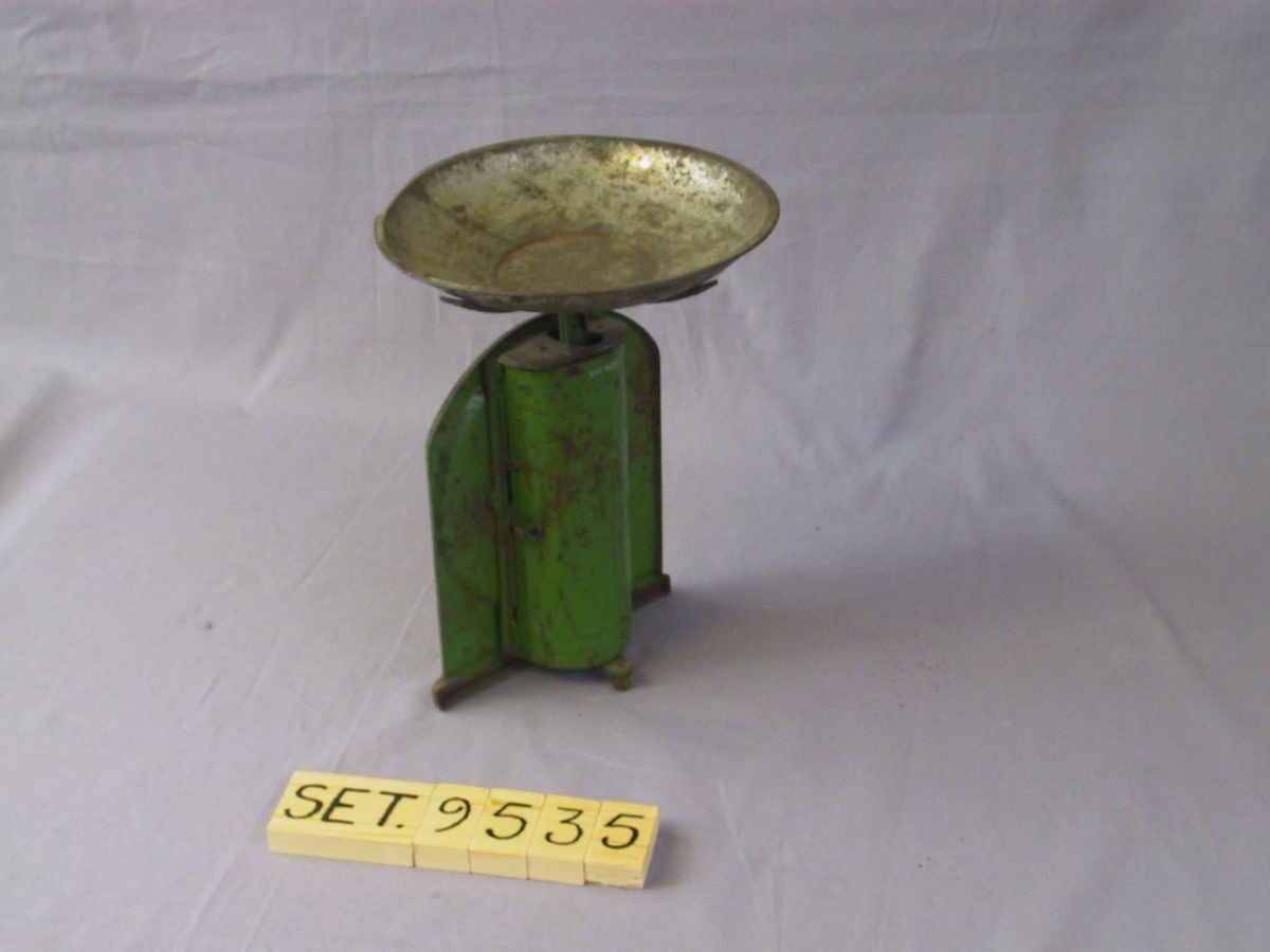 Flat framside med rett botn og rette sider, avrunda topp. Kvit, klokkeforma talskive med vektskala og visar. Laus skål som står på kryssforma, flate berepinnar på toppen av stav som går ned i halvsylinderforma bakstykke. Grønmåla med kvit talskive og svarte tal.