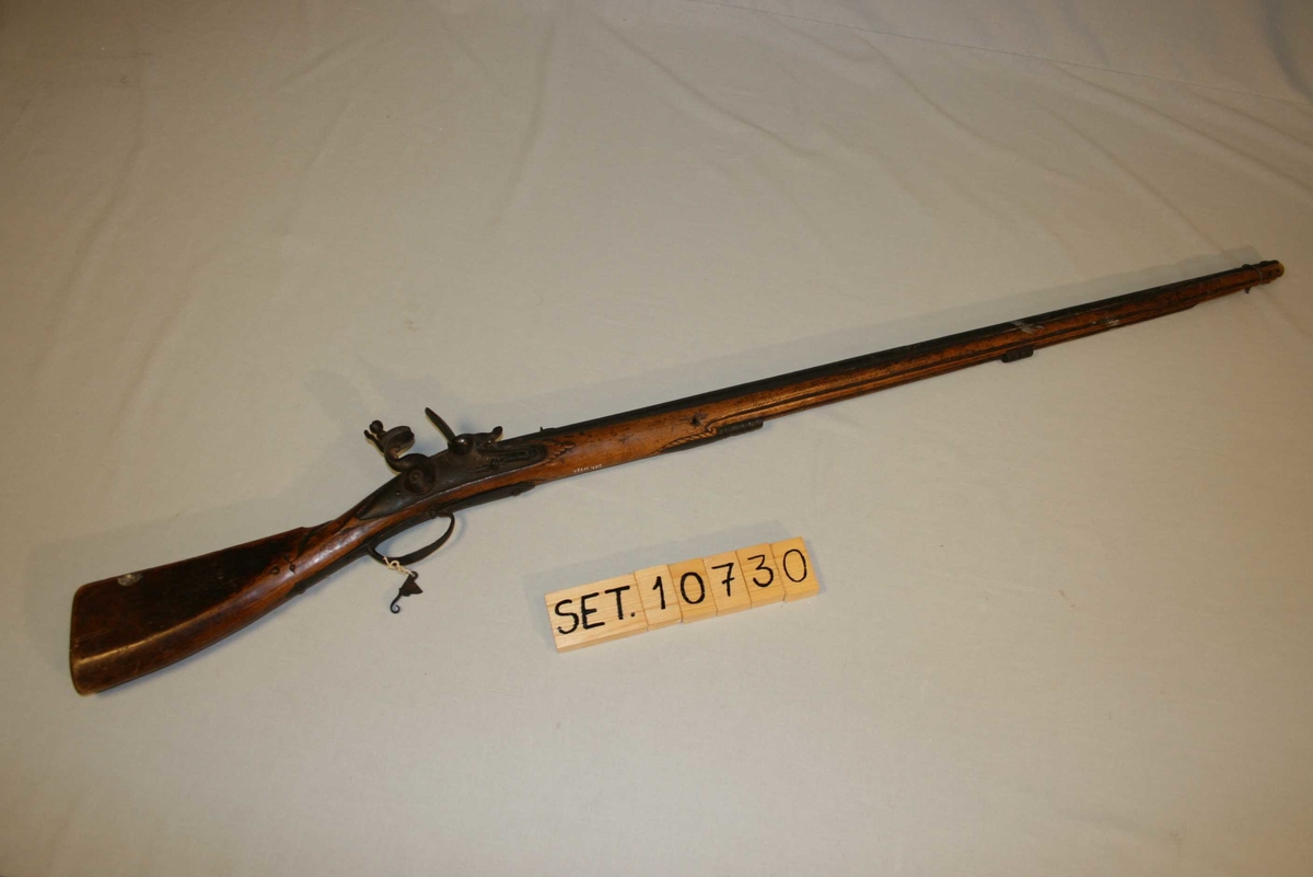 Flintlåsgevær med glatt pipe. Kolben dekorert med treskurd. 