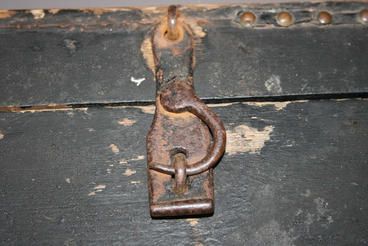 Rektangulær trekasse med hengsla, flatt lok. Jernbeslag på hyrna, 2 av dei opprusta nedanfrå. Uoriginal botn. Jernhempe med krok til å feste loket. Svartmåla (tjøra?) Sprekk i loket, hol i bakveggen.