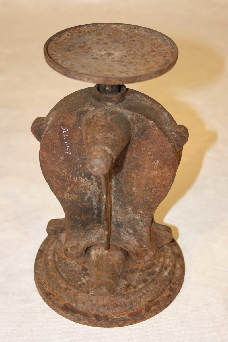 Rund fotplate, metall. Klokkeforma talskive med vektskala i gram og kilo, med visar. Sjølve talskiva av messing. Rund plate på toppen, manglar skål. Rusta.