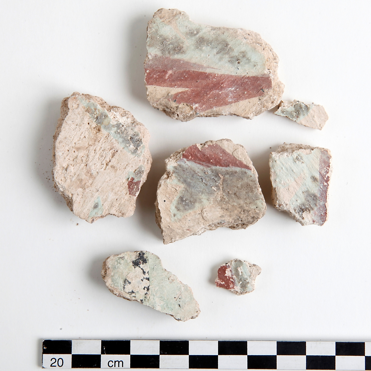 Fragment av kalkputs. Bemålade kalkputsfragment med schablonmotiv samt heltäckande färger i rött, grönt/turkos, gult, orange, svart, och brunt. Datering sent 1400-tal.