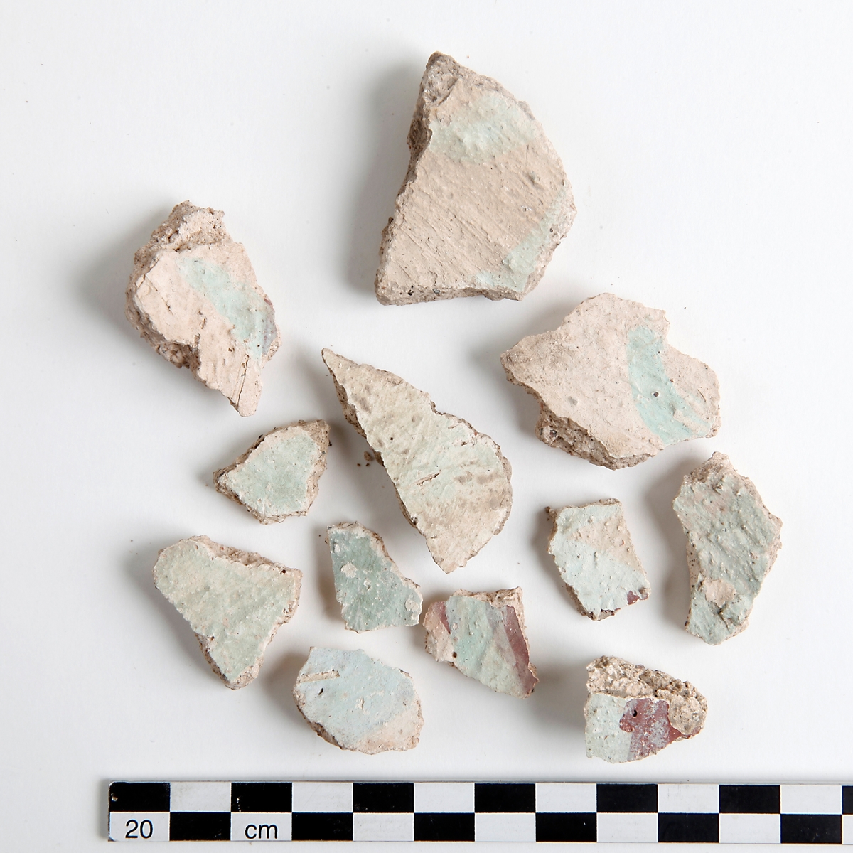 Fragment av kalkputs. Bemålade kalkputsfragment med schablonmotiv samt heltäckande färger i rött, grönt/turkos, gult, orange, svart, och brunt. Datering sent 1400-tal.