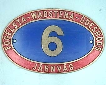 Oval lokskylt av mässing målad i rött och blått.
Skylten kommer från ånglok nr 6 från Fogelsta-Wadstena-Ödeshögs järnväg.

FVÖJ Nº 6 SEXAN
MÖJ Nº 106 (1919 - 1950)
SJ Np 3156 
Motala Verkstad Nº 484